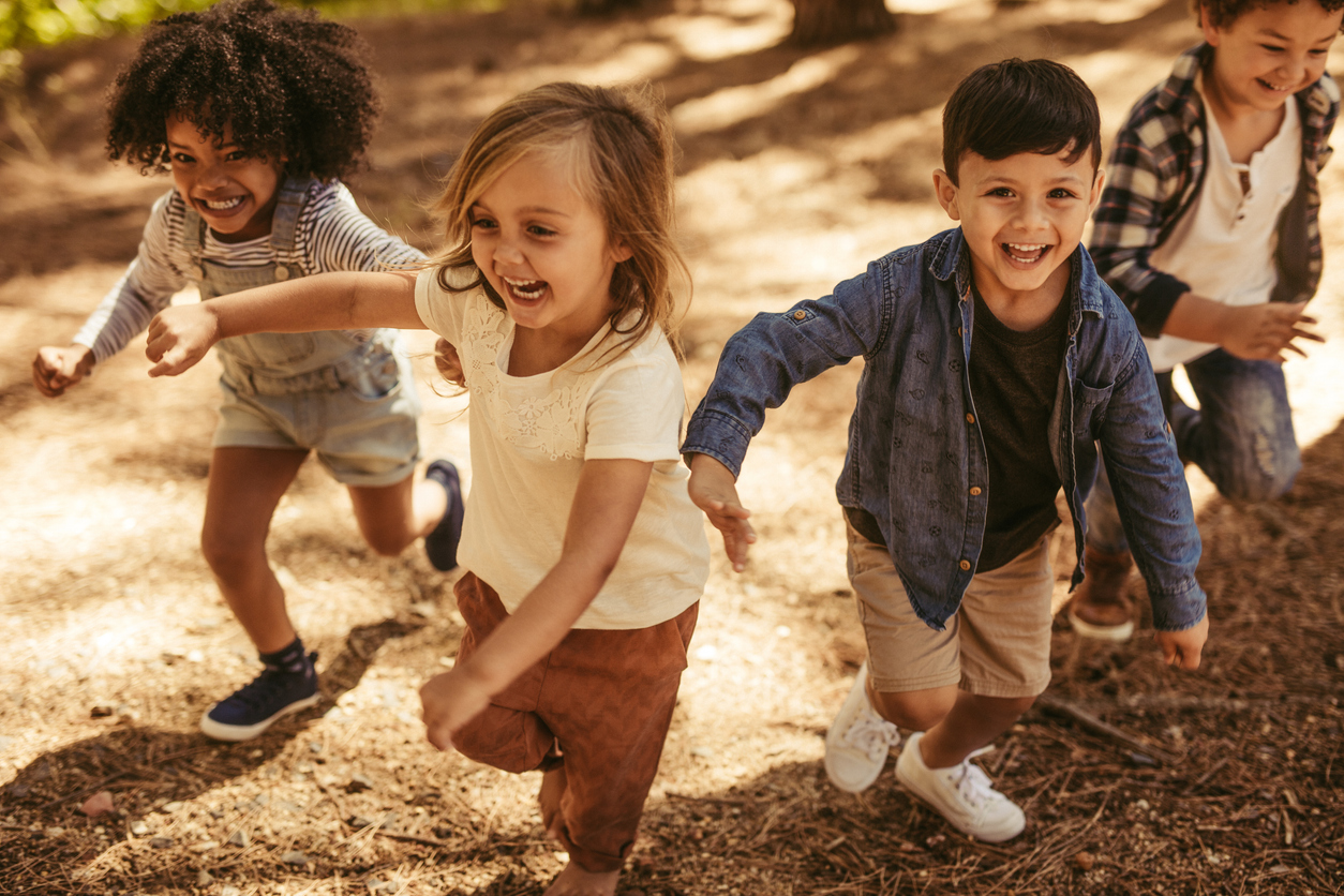 Adorable kids running up hill in a park. Group of children playing together in forest.